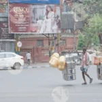 Man carrying a large number of containers walking across a street - Log, colour and B&W