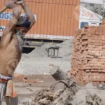 The man is using an axe to chop into a large log, creating wood chips and sawdust - Log, colour and B&W